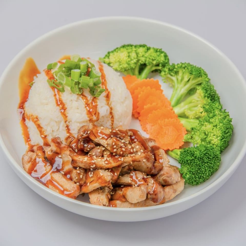 Teriyaki chicken with white rice, green onions, broccoli, and carved carrots in a white bowl.
