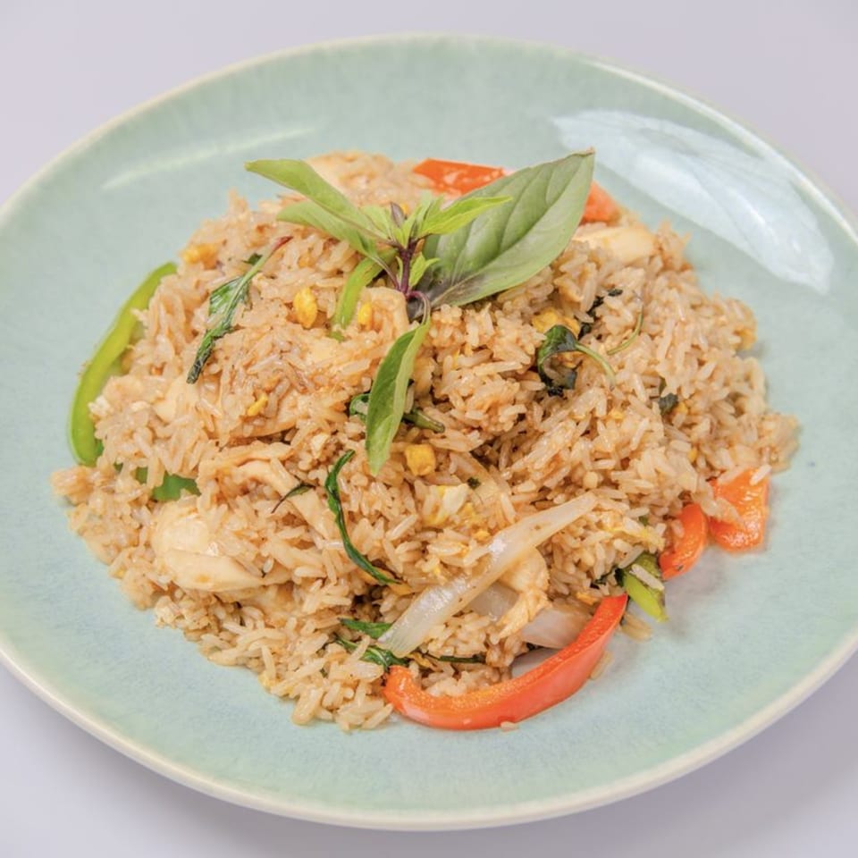 Thai fried rice with chicken, bell peppers, onions, and basil on a light green plate.