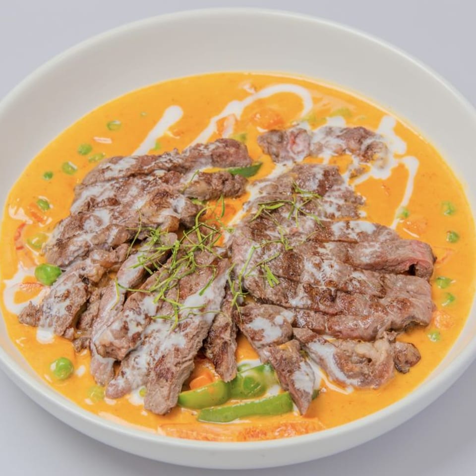 Thai red curry with sliced beef, green vegetables, and a drizzle of coconut milk.