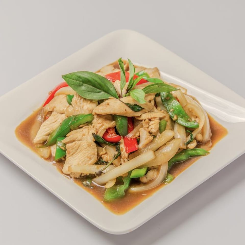 Thai basil chicken stir-fry with green beans, red peppers, and onions on a white plate.